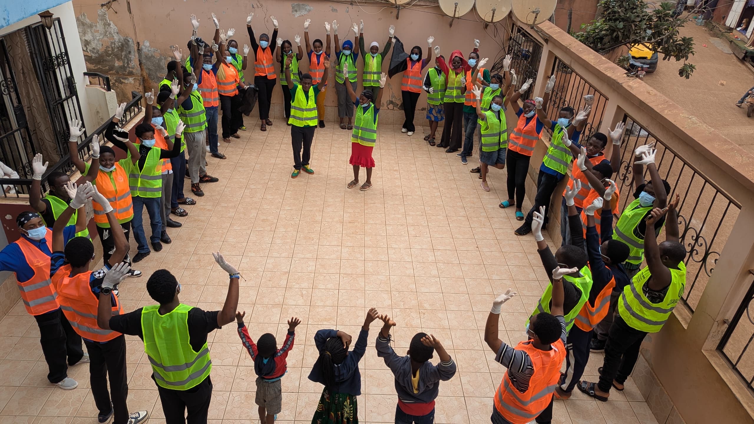 About 30 youths in circle with Blaise in the middle all wearing building worker green aprons as they participate in building WiseBoxes